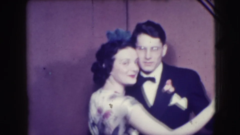The Joliet home-movie frame shows the couple mid-dance, her arm around him and his tuxedo boutonniere visible.