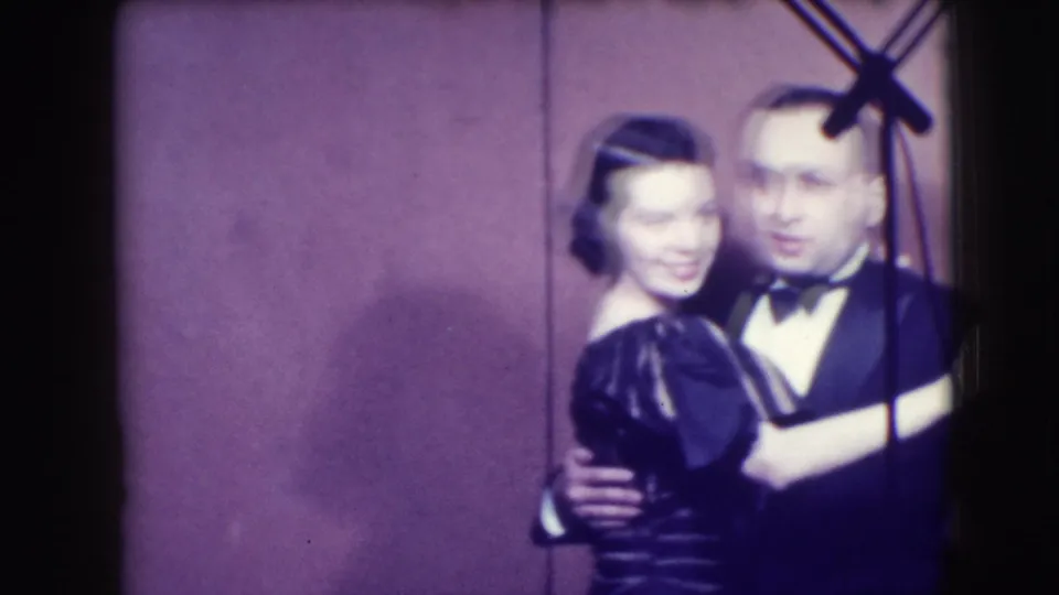The 1941 Joliet home movie shows the woman smiling while the man in a tuxedo holds her during a slow dance.