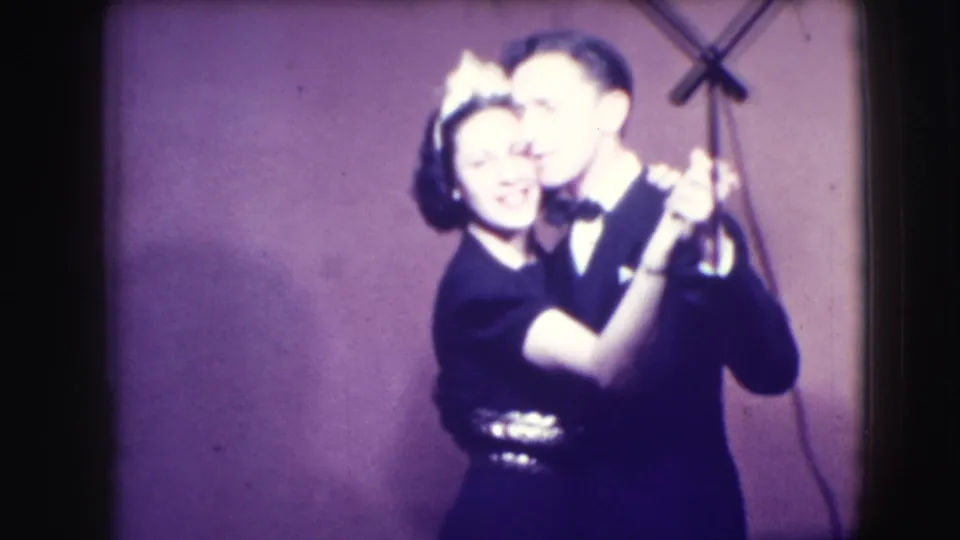 A smiling couple in formal clothing dances near a visible stand in 1941 Joliet, Illinois home-movie footage.