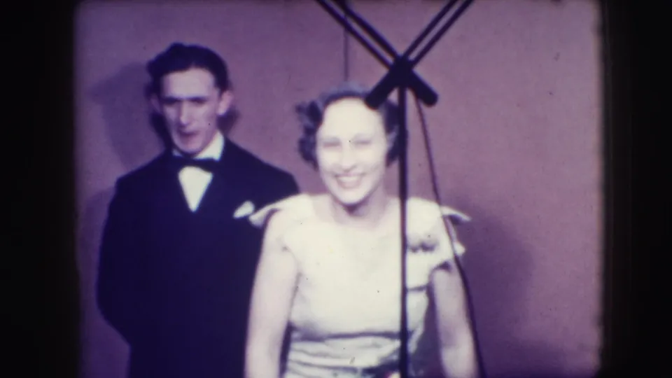 At the end of the 1941 Joliet, Illinois clip, the tuxedoed man stands behind a smiling woman beside a visible microphone stand.