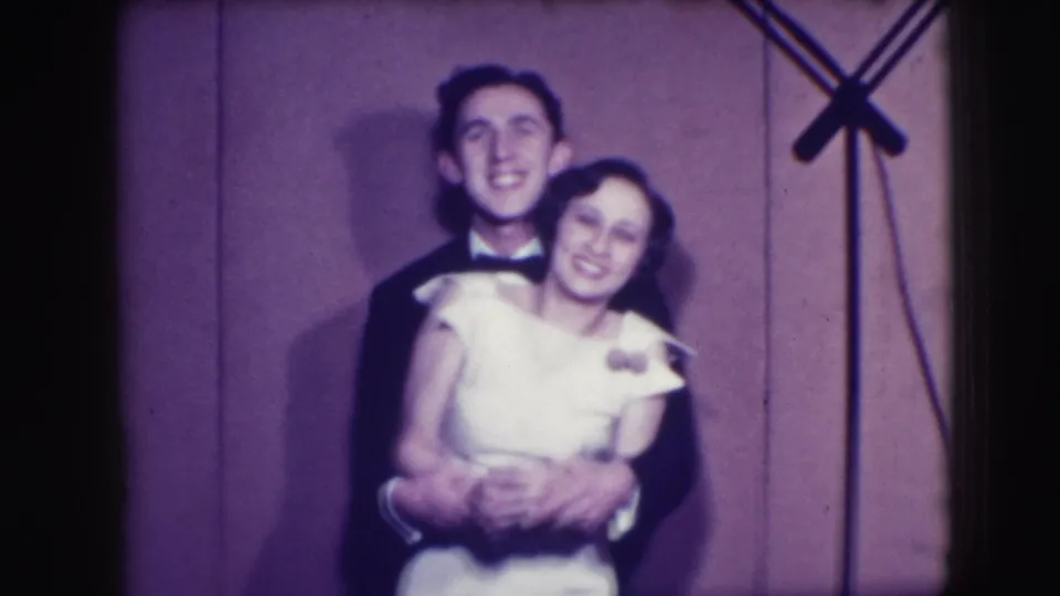 A young formalwear couple leans together and smiles in the 1941 Joliet home movie, their clasped hands visible near the woman's waist.