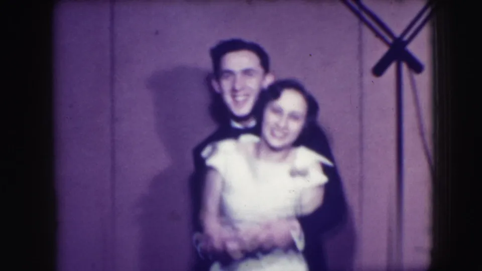 The couple remains in a smiling embrace in the 1941 Joliet 8mm clip, framed softly with a purple cast and a stand along the side.