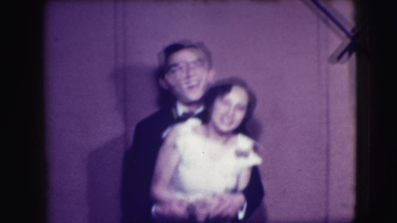 Blurred adult couple dancing in formal wear against a plain backdrop.