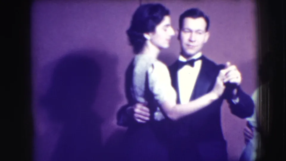 1941 Joliet home-movie frame of an adult couple in formal wear dancing close together against a plain backdrop.