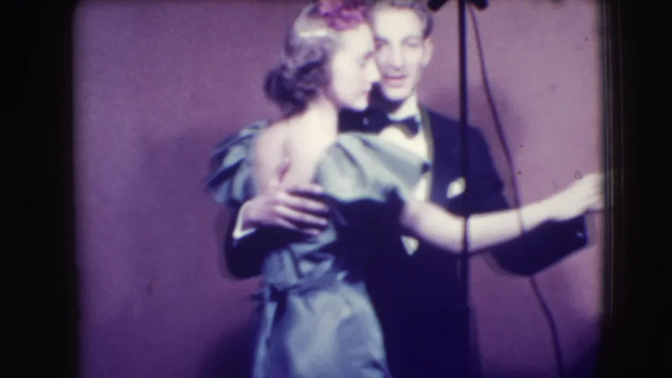 A woman in a light satin-like dress dances with a tuxedoed man in the Joliet 1941 home-movie scene, with a vertical cord visible at right.