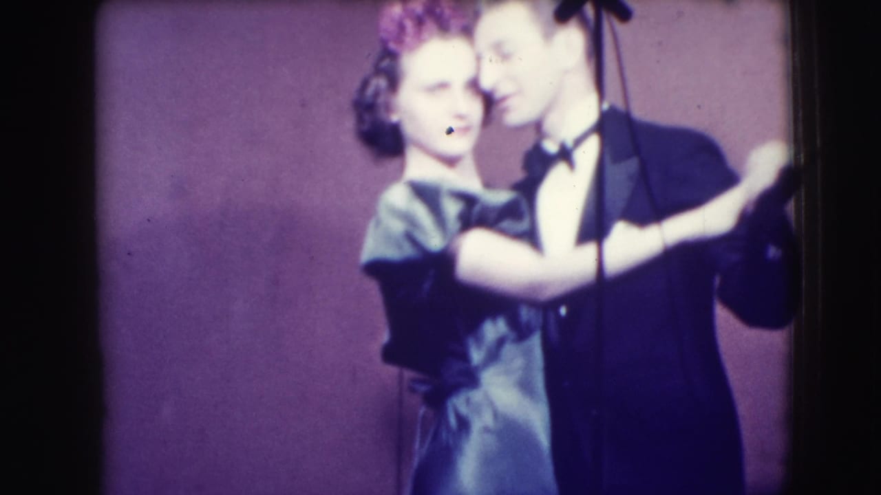 1941 Joliet, Illinois 8mm frame of a formal couple dancing cheek to cheek on a small stage with a microphone stand nearby.