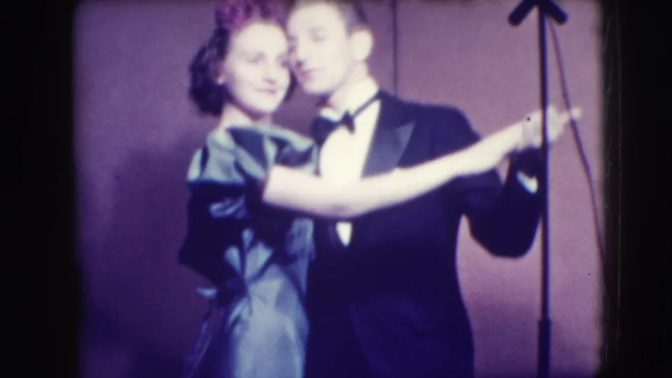 The couple faces toward the camera in a close dance hold, with the 1941 Joliet stage backdrop and microphone stand still visible.