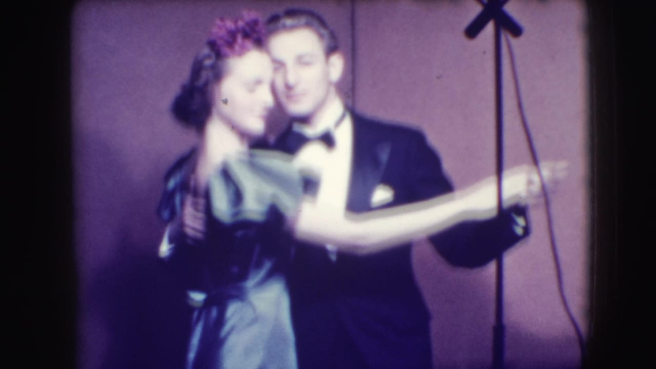 Couple in formal dress dancing closely under purple lighting.