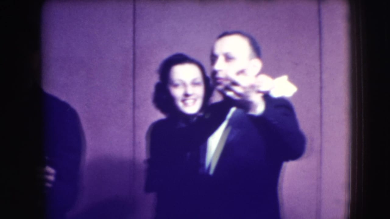 Adult couple in formal attire slow dancing against a plain backdrop.