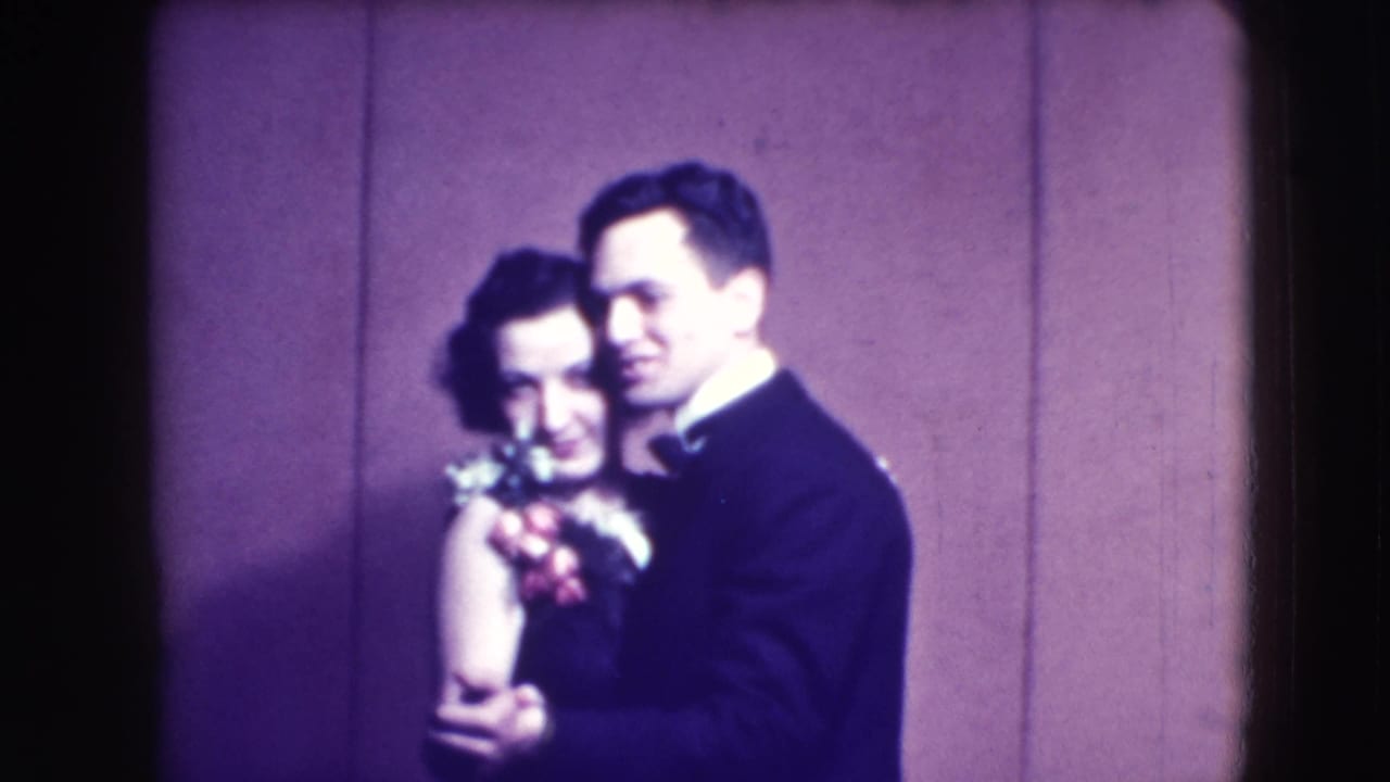 Couple swaying together, with the woman holding flowers near her shoulder.