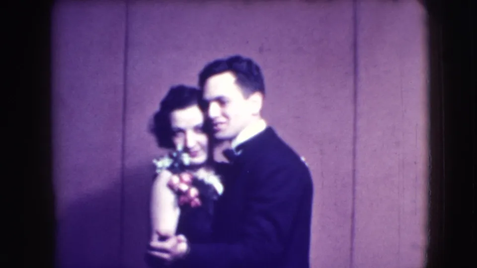 The couple continues a close dance in the 1941 Joliet 8mm scene, framed softly against a purple-toned wall.