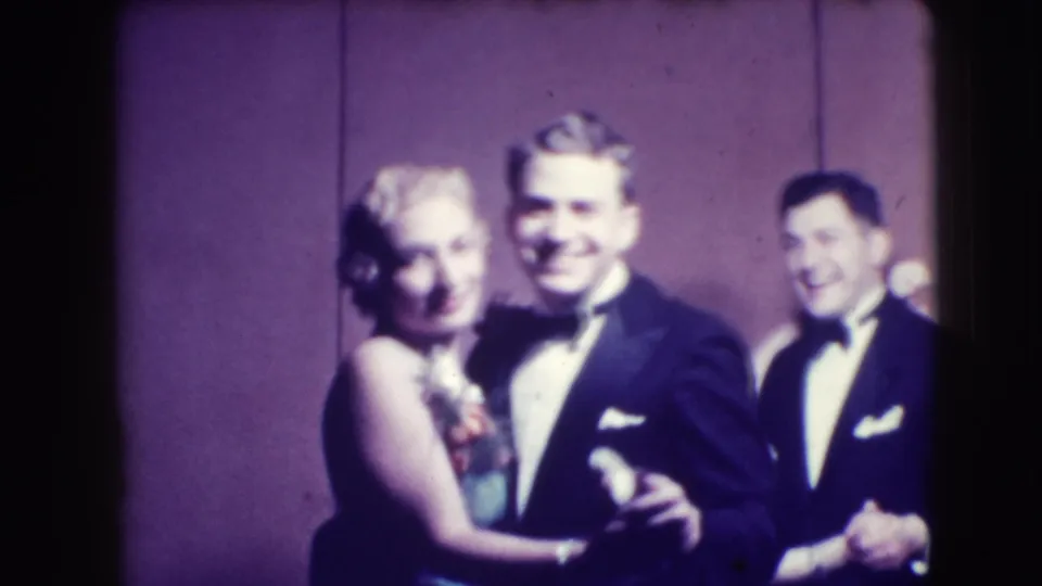 Two couples in tuxedos and evening gowns smile while dancing in the 1941 Joliet indoor home-movie scene.