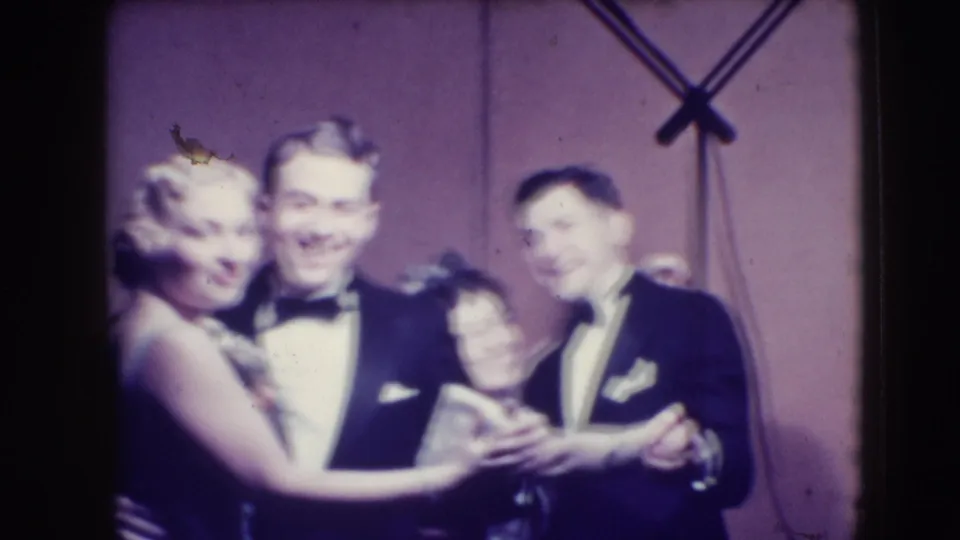Three adults in tuxedos and an evening gown appear mid-dance in soft 8mm focus during the Joliet formal party footage.