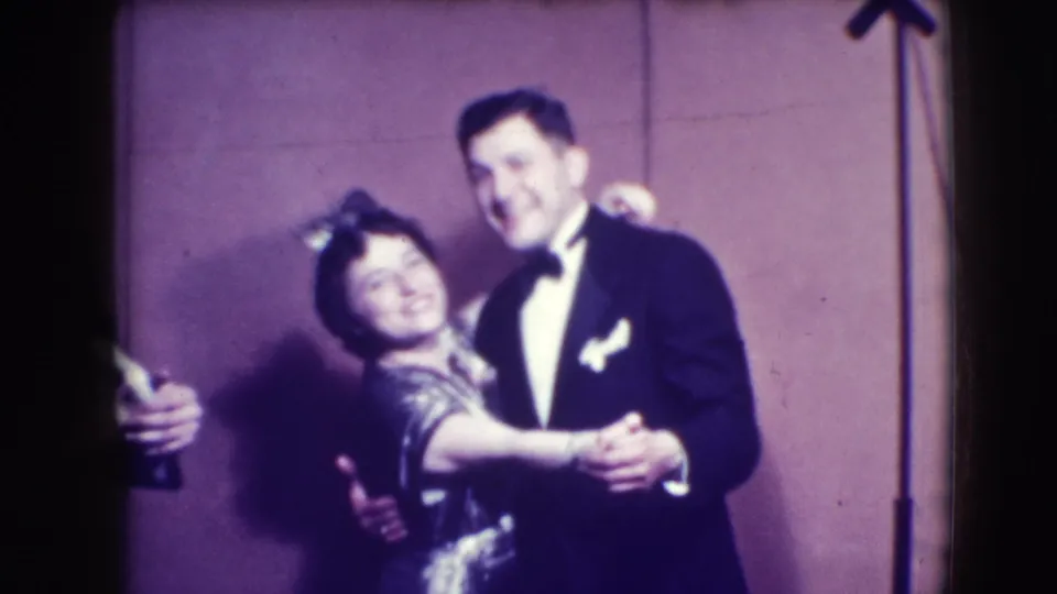 A woman in a patterned dress leans toward her tuxedoed partner during a dance in the 1941 Joliet home-movie scene.