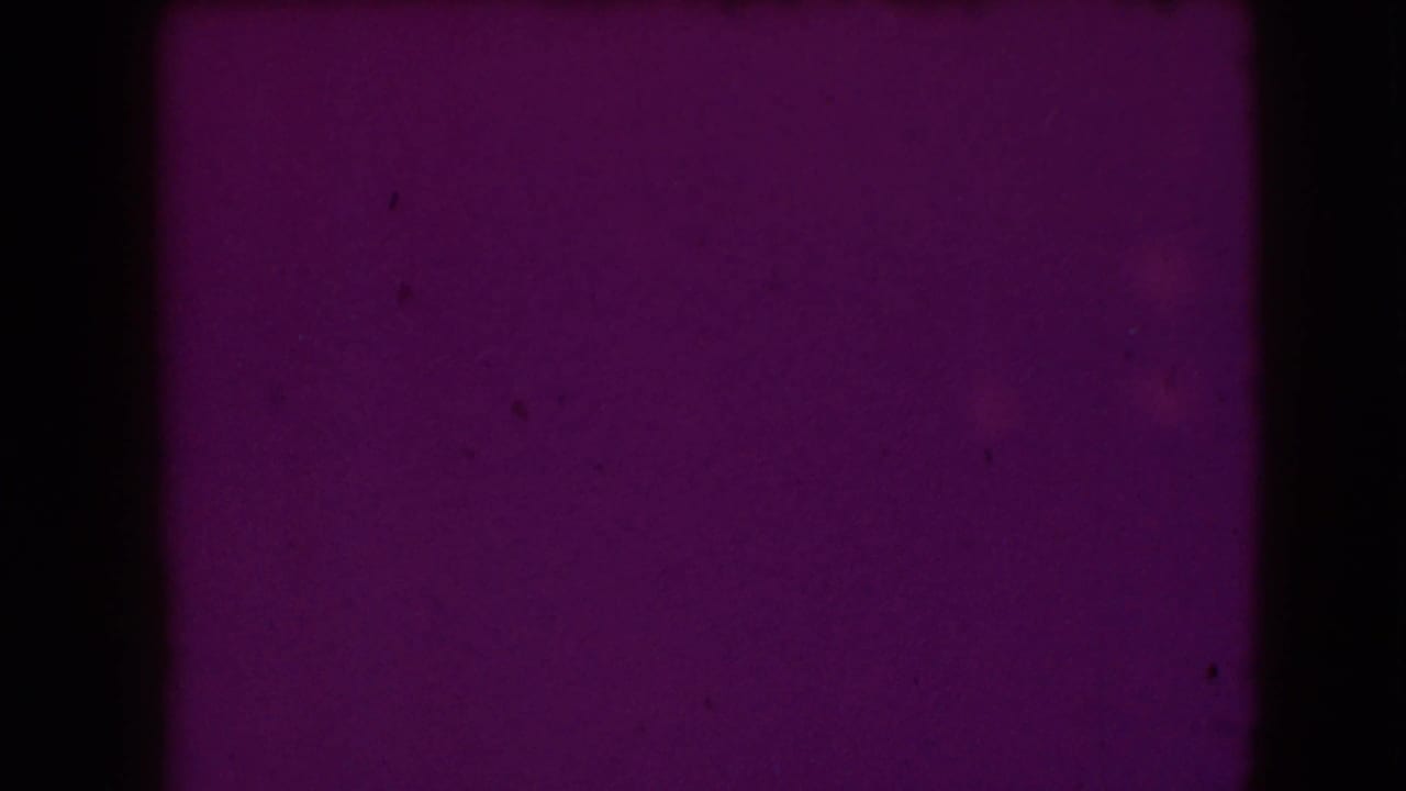 Purple-tinted film frame with mostly blank wall and dark film edge.