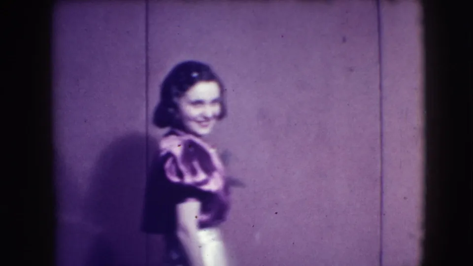 This 1941 Joliet home-movie frame shows a tuxedoed man dancing with a woman in a patterned dress near a plain wall.