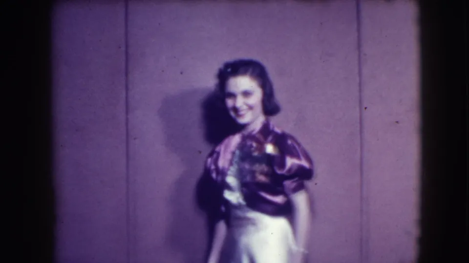 The woman continues posing in a shiny pink evening dress, smiling toward the camera in the Joliet, Illinois home-movie clip.
