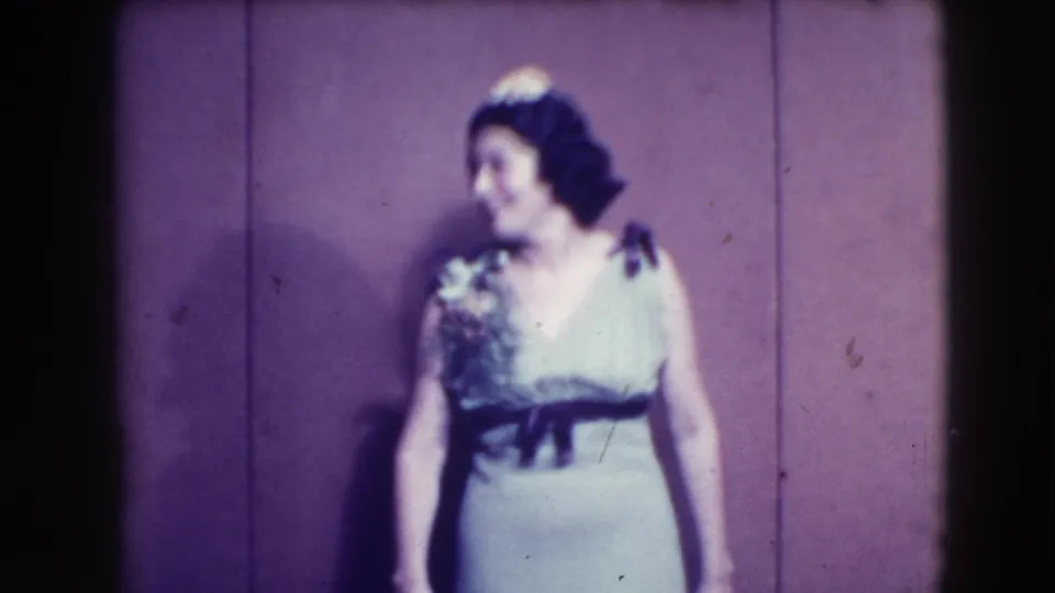 A woman models a pale blue or light-colored gown with a dark sash, turning sideways against the plain backdrop in the 1941 clip.