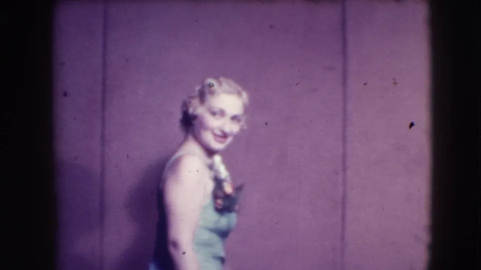 A blonde woman in a light-colored dress smiles and poses in the same 1941 Joliet stage setting.