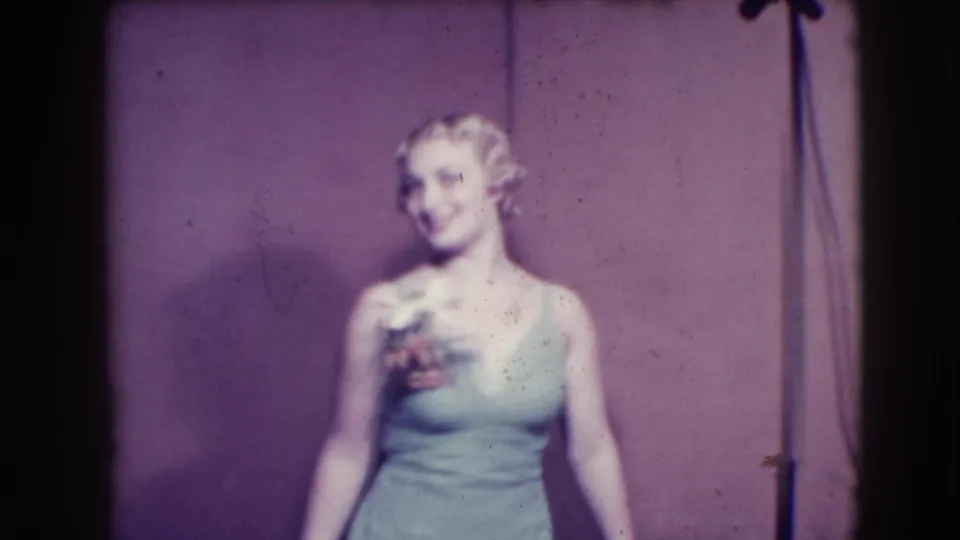 In Joliet, Illinois, a woman in a light sleeveless dress smiles toward the camera during a 1941 stage presentation.