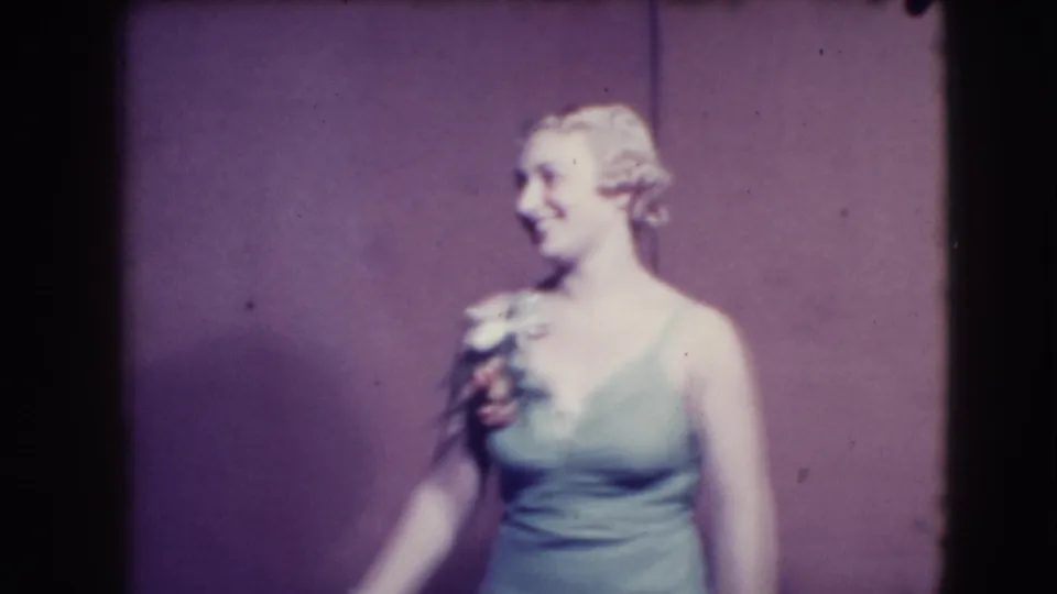 The woman in the light dress turns to the side on a Joliet stage, holding flowers in 1941 home-movie footage.