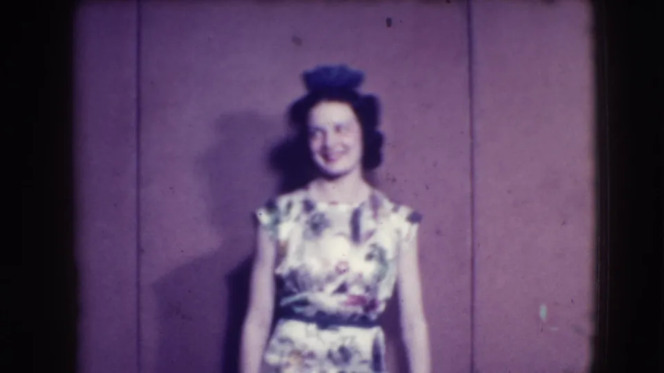 The floral-dressed woman remains on stage, smiling toward the camera in the 1941 Joliet home-movie scene.