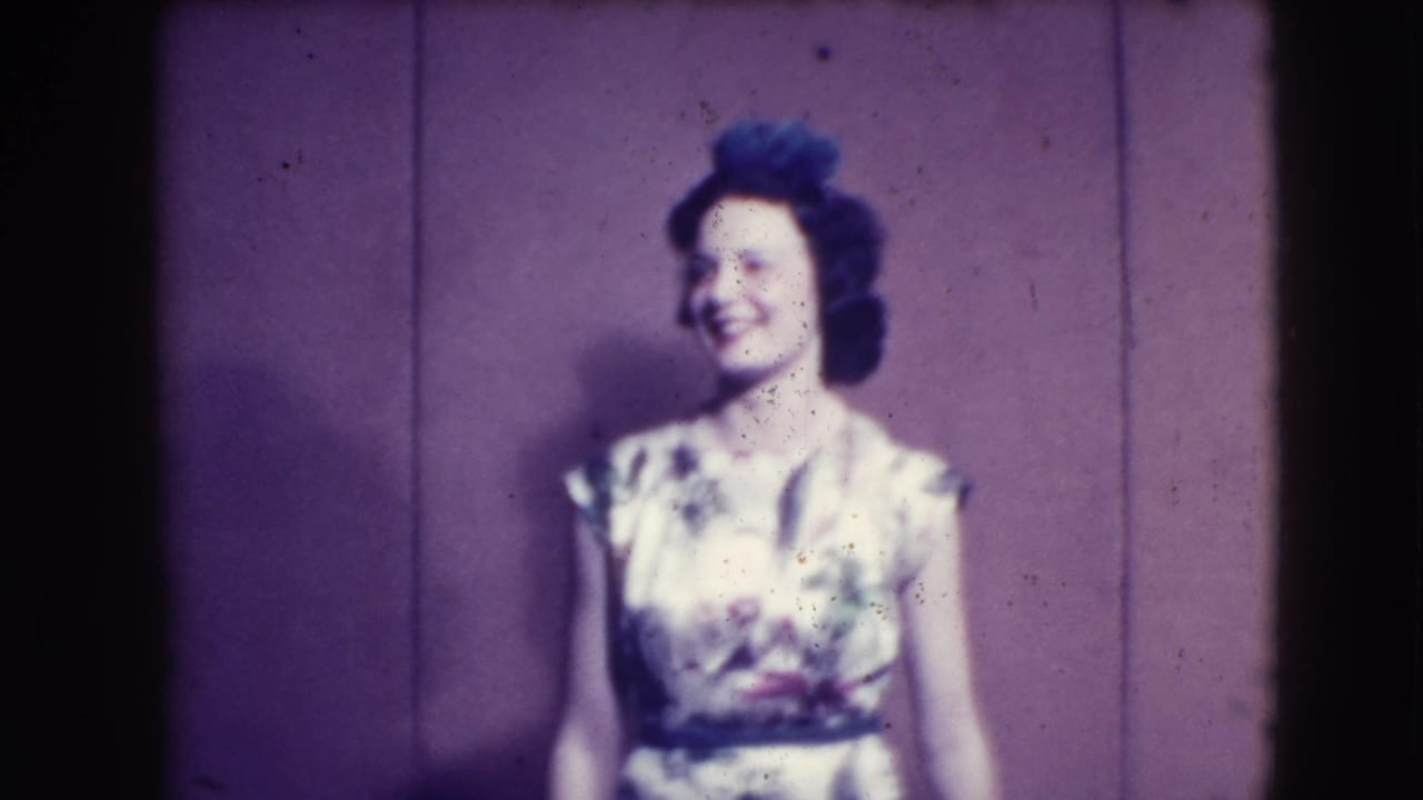 Woman in a light floral dress smiles while standing before a purple backdrop.