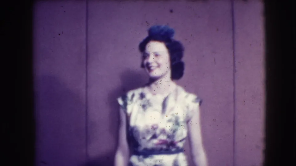 In this 1941 Joliet, Illinois 8mm frame, a woman in a light floral dress smiles against a purple indoor backdrop.