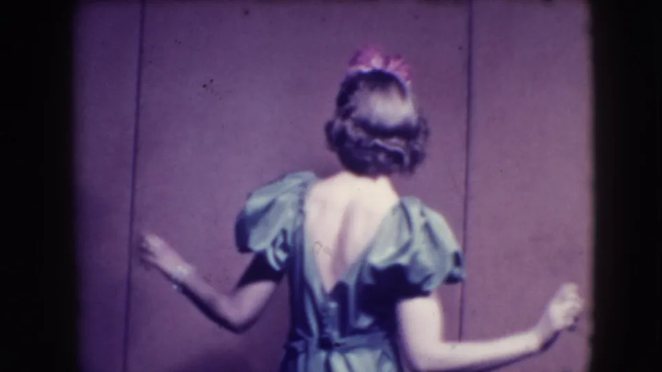 The woman turns her back to the camera, showing the rear neckline and puffed sleeves of the green dress against the purple backdrop.