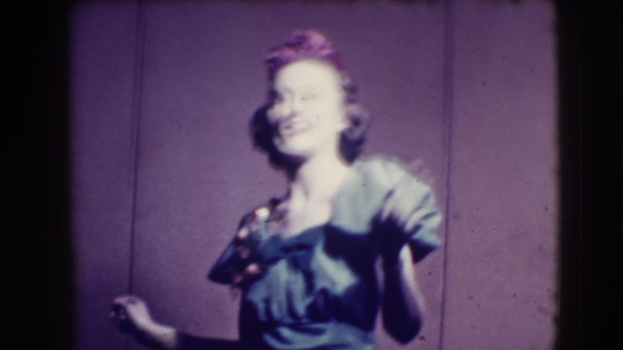 Woman in a dark dress smiles while turning before a plain purple backdrop.