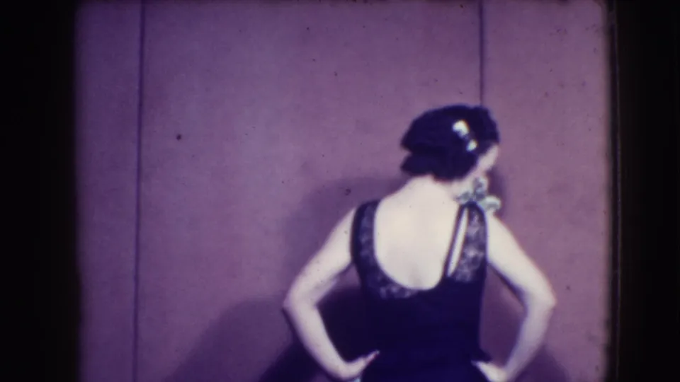 Woman in 1941 Joliet footage turns to show the back of a dark sleeveless dress with lace detail near the shoulders.