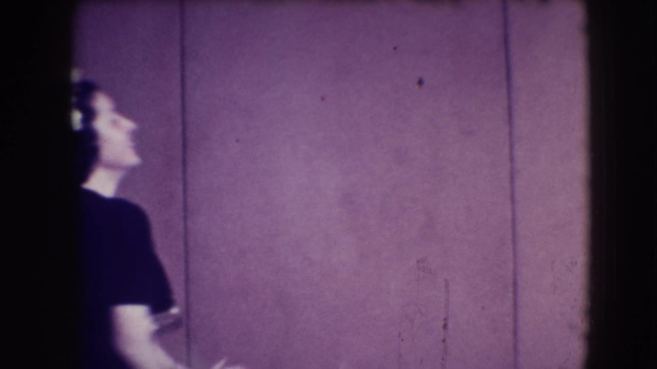 Woman in a dark dress partly turned beside a purple-paneled wall.