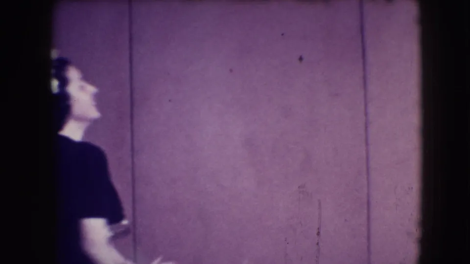 In 1941 Joliet home-movie footage, a woman in a dark dress is partly visible while turning near a purple-paneled wall.
