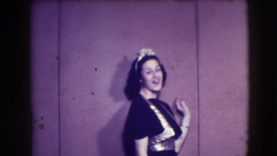 A smiling woman in a dark dress with bright trim and a decorative headpiece poses in the 1941 Joliet home-movie frame.