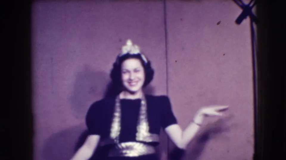 The woman faces the camera in a dark trimmed dress and headpiece, smiling and gesturing in 1941 Joliet home-movie footage.