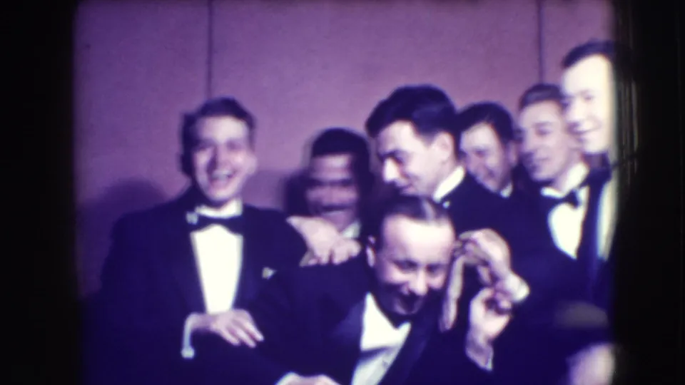 Men in tuxedos cluster together, with one man bending forward laughing as others smile behind him at the 1941 Joliet event.