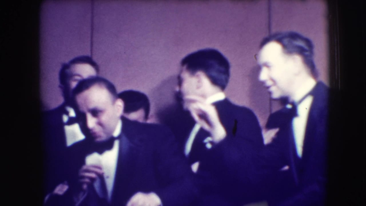 Adult men in tuxedos and bow ties gather indoors in Joliet, Illinois, in a 1941 home-movie frame, several reacting playfully toward the camera.