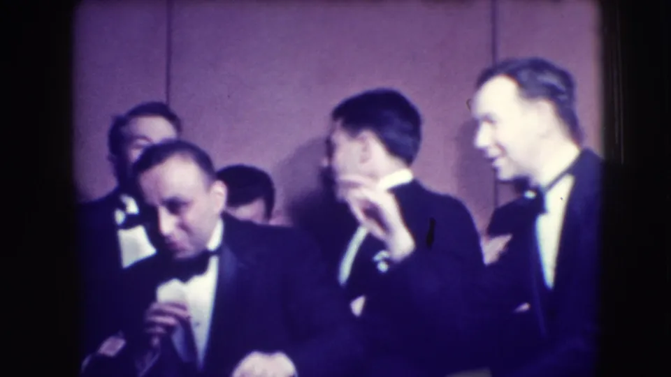 Adult men in tuxedos and bow ties gather indoors in Joliet, Illinois, in a 1941 home-movie frame, several reacting playfully toward the camera.
