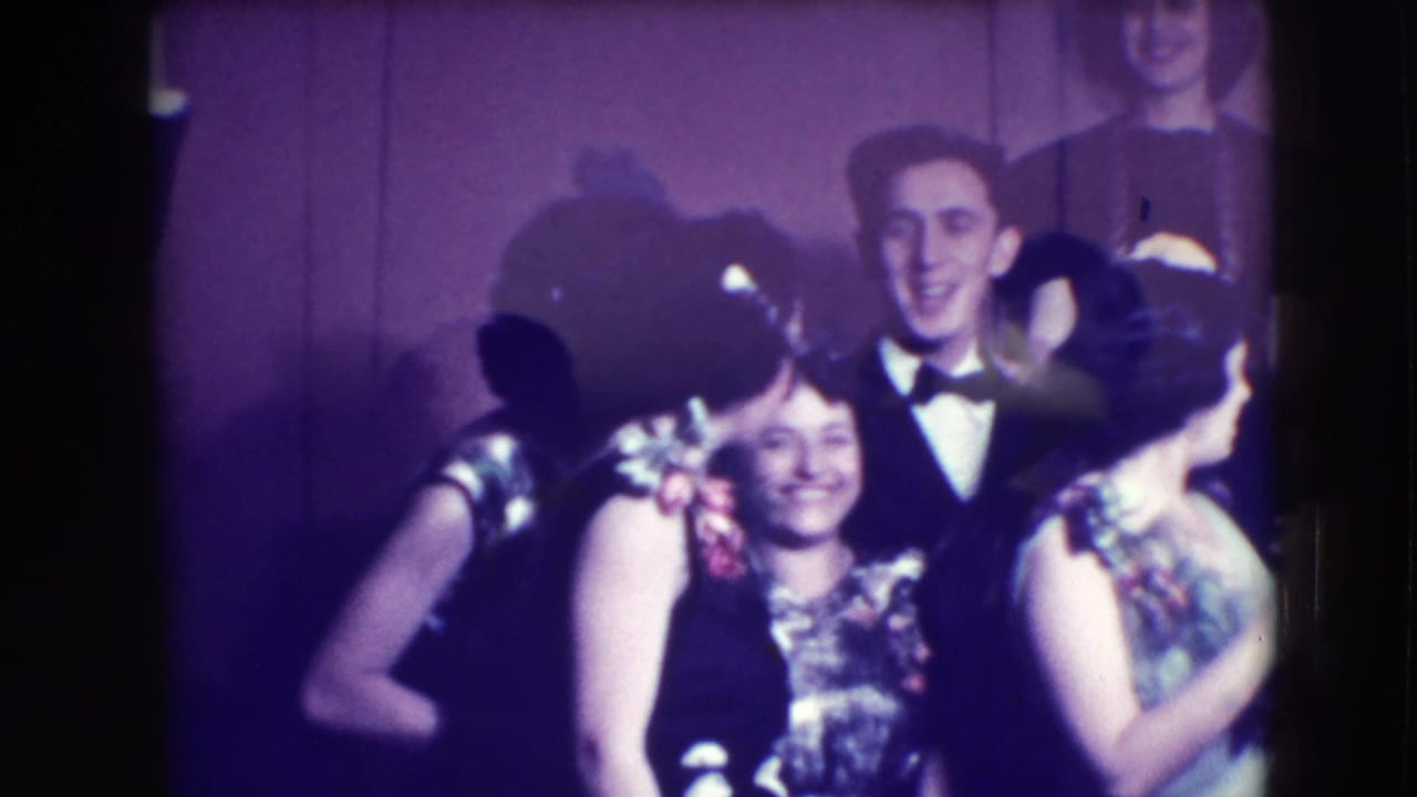 Young adults in formal clothing gather closely and smile while posing indoors.