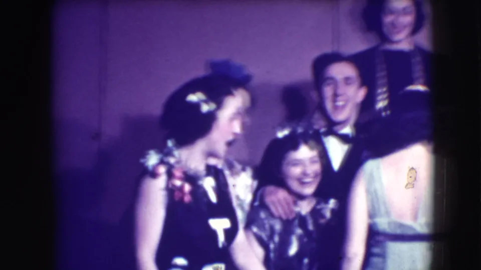 Formally dressed young adults in Joliet, Illinois laugh and lean into a tight group pose for the 8mm camera.