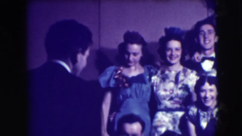 A man with his back to the camera faces a smiling group of formally dressed young adults in this Joliet 8mm scene.