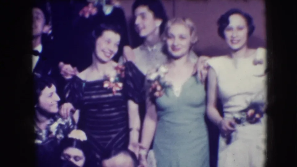 The 8mm frame shows women in black, pale green, and white formal dresses posing at a Joliet party in 1941.