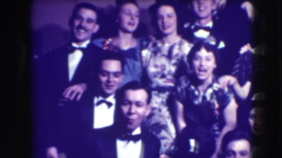 Adults in tuxedos, patterned dresses, and eveningwear pose in a soft 8mm frame from the 1941 Joliet formal event.