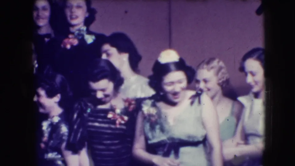 Joliet 1941 home-movie frame of young women in formal gowns and corsages laughing in a crowded prom group.