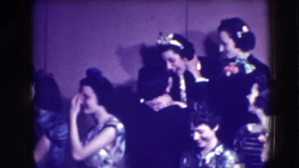 Adults at a 1941 Joliet formal gathering laugh and lean toward each other, with eveningwear and corsages visible in soft 8mm color.