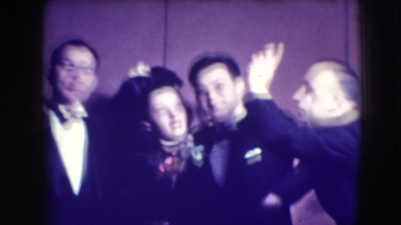 Adults in formal clothing crowd together and pose against a plain wall.