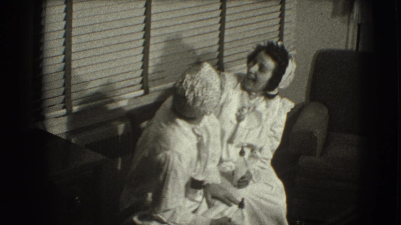 Woman in a white dress and hat sits beside a smaller bonneted figure near window blinds.