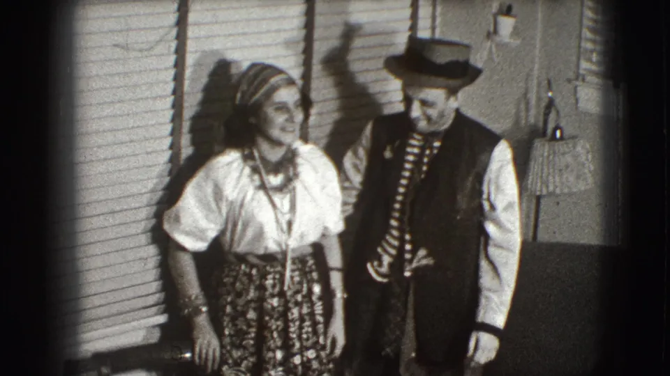 In Joliet, Illinois home-movie footage from 1941, two adults in theatrical costumes pose near window blinds and a floor lamp.