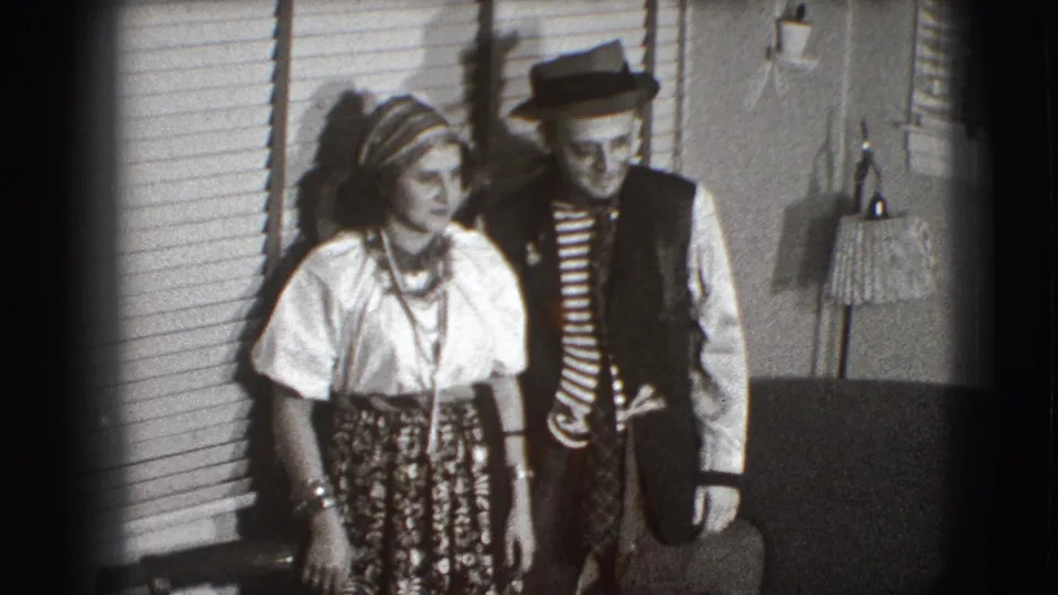 Two adults in 1941 Joliet home-movie footage pose in vaudeville-style costumes, with the man in a fedora and striped shirt.