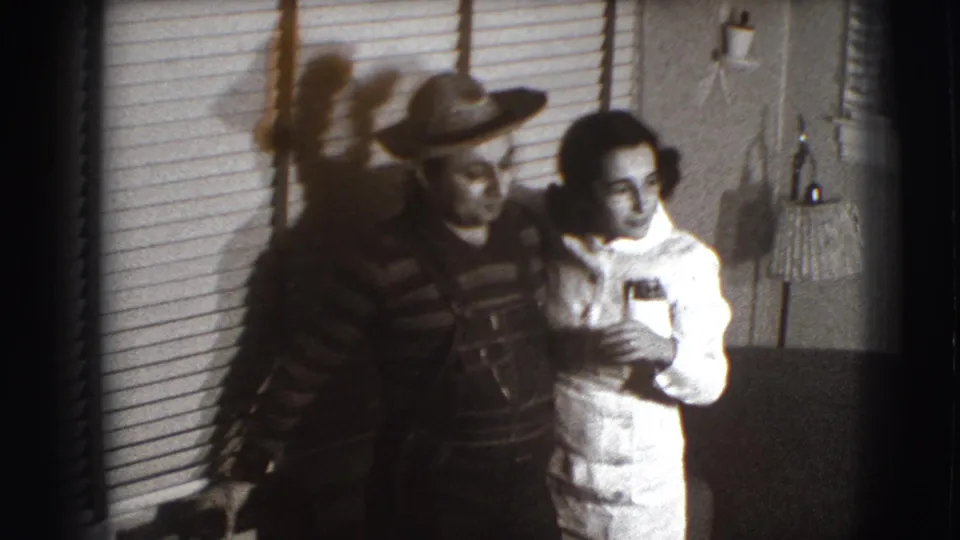 Another costumed pair appears in the same 1941 Joliet interior, standing close beside blinds, a lamp, and an upholstered chair.